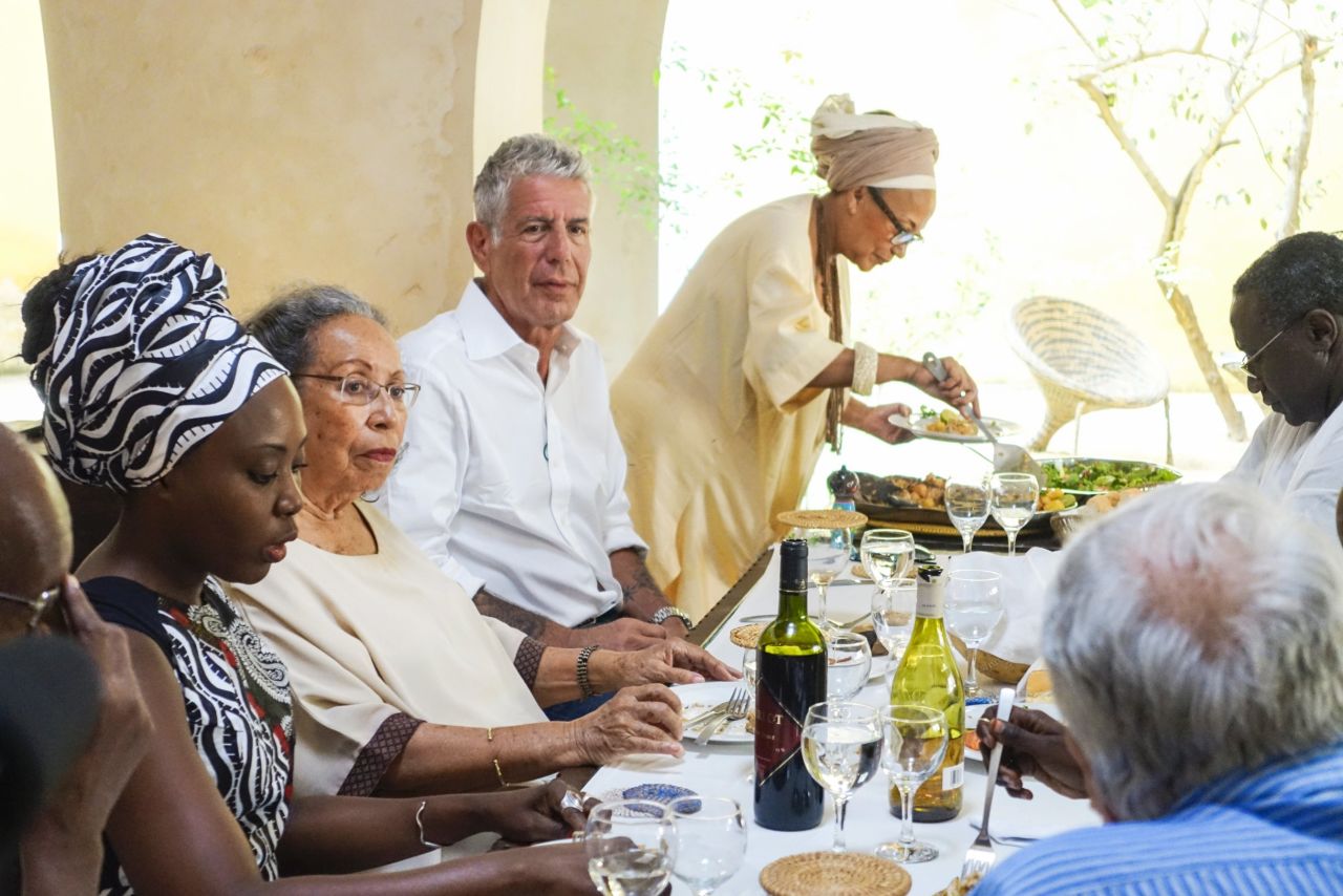 Bourdain enjoys a garden party meal hosted by Marie-Caroline Camara (far right) at her bed and breakfast, "Au Fil du Fleuve" in Saint-Louis. Camara has worked to preserve some of the city's beautiful historic architecture. 