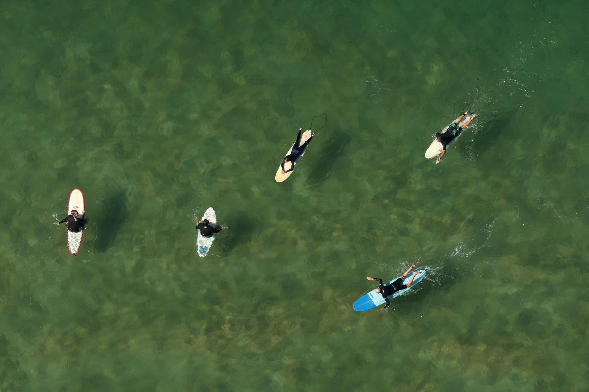 Surfers paddle their boards and cast shadows on the seabed at Avalon Beach.