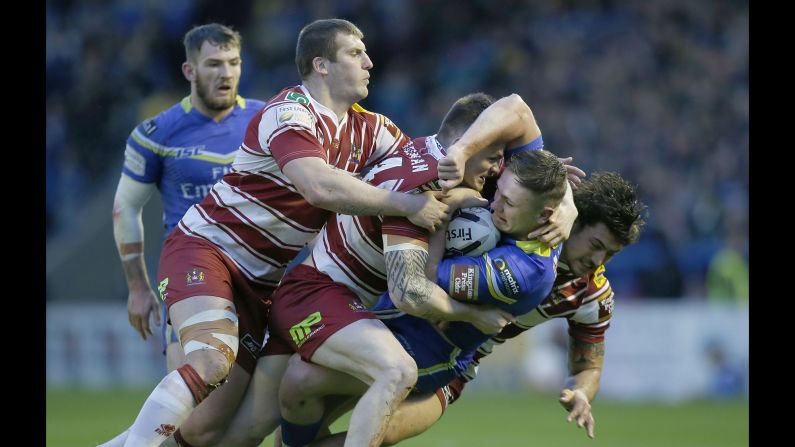 Ben Currie of the Warrington Wolves is gang-tackled by Wigan players during a Super League match in Warrington, England, on Thursday, April 28.