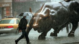 NEW YORK, UNITED STATES:  A pedestrian passes in front of a statue of a bull in the Wall Street area in New York City where rains from Hurricane Floyd hit 16 September, 1999.  Floyd made landfall in Wilmington, NC and Federal Emergency Management Agency chief James Lee Witt said 16 September 1999 that this is a major disaster for North Carolina. (Photo credit should read DOUG KANTER/AFP/Getty Images)