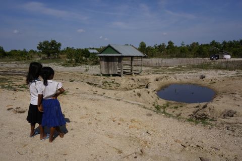 Two schoolgirls look at a stagnant pond. They have no choice but to wash in it and often suffer skin conditions and risk malaria as a result.