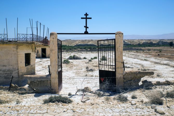 The rusted gate of the Russian Orthodox church looks out onto the Jordan River and the Jordanian mountains beyond. After the fields are cleared, each church will have its own walking path to the river.