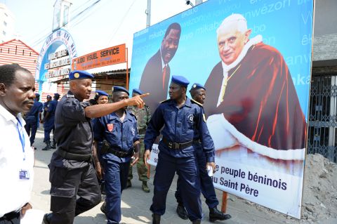 Policemen in Benin walk past a sign announcing a mass conducted by Pope Benedict XVI during his visit in 2011. <br />
