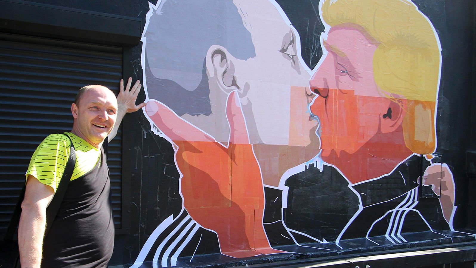 A man poses next to a mural on the wall of Keule Ruke depicting U.S. Presidential hopeful Donald Trump and Russian President Vladimir Putin greeting each other with a kiss in the Lithuanian capital of Vilnius on May 13, 2016.