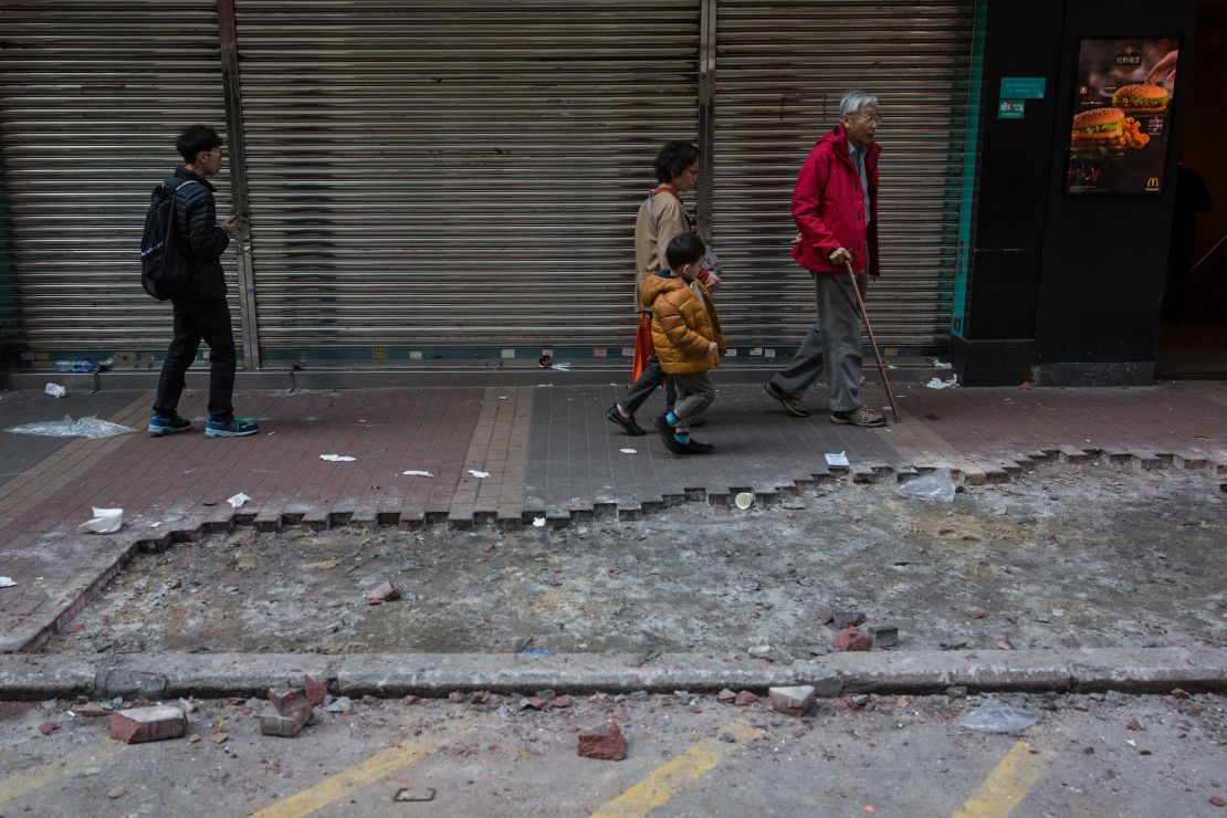 People walk past debris and a section of the pavement which was partially ripped up and used in overnight clashes between protesters and police in the Mongkok area of Hong Kong on February 9, 2016.