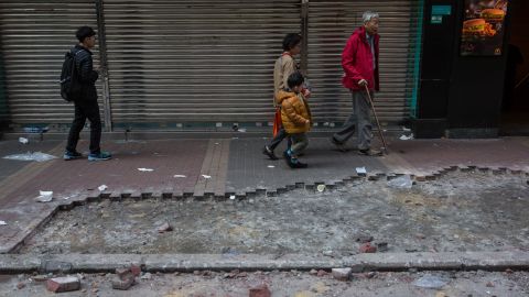 People walk past debris and a section of the pavement which was partially ripped up and used in overnight clashes between protesters and police in the Mongkok area of Hong Kong on February 9, 2016.