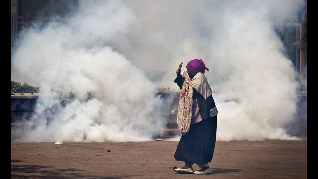 An elderly woman caught up in the clashes holds her hands in the air as a riot policeman approaches amid clouds of tear gas. 