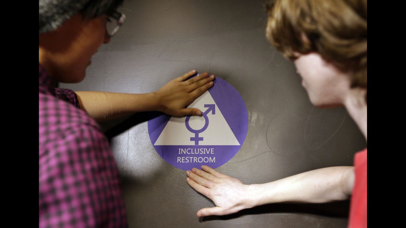Destin Cramer, left, and Noah Rice place a new sticker on the door of a gender-neutral bathroom at Seattle's Nathan Hale High School on Tuesday, May 17. Since 2012, Seattle has mandated that transgender students be able to use the bathrooms and locker rooms of their choice. 