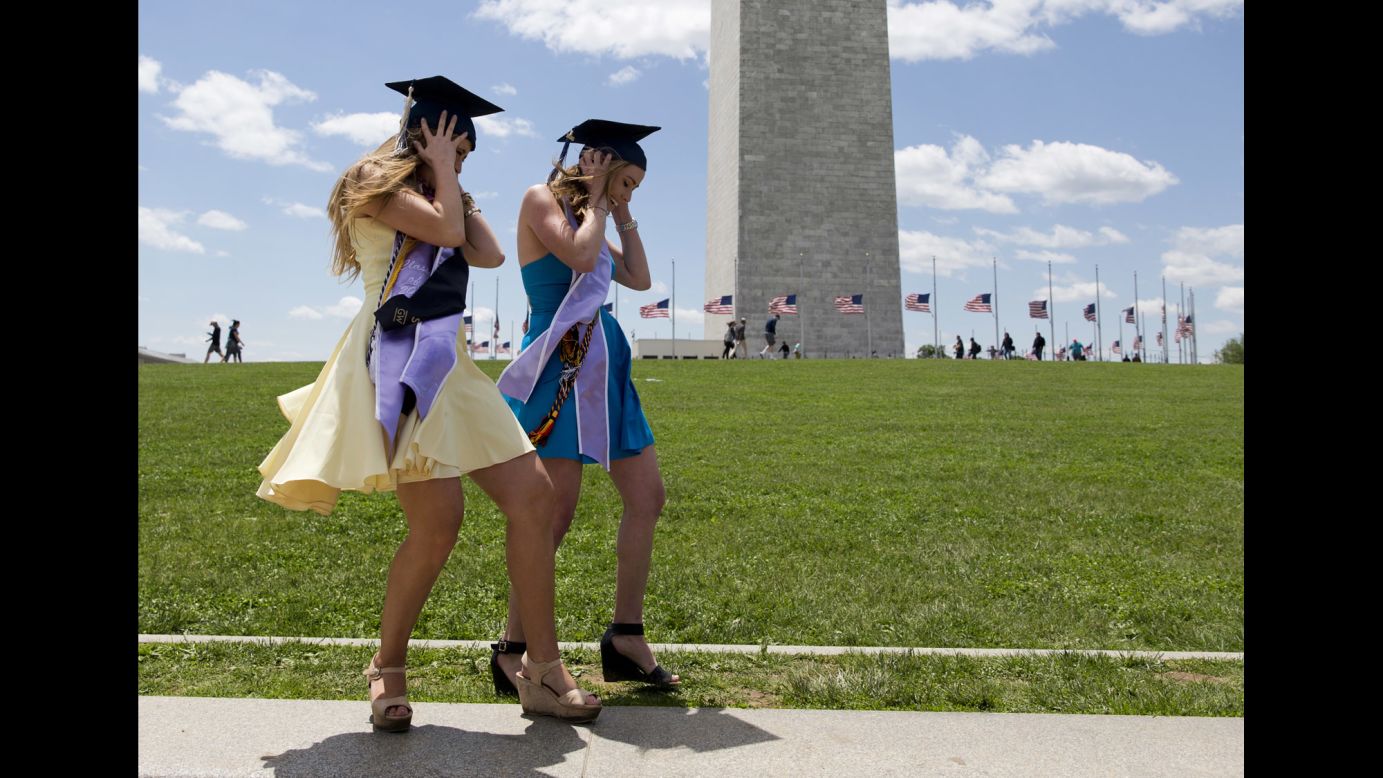 Two graduates of George Washington University struggle against the wind as they pose for photos near the Washington Monument on Sunday, May 15.