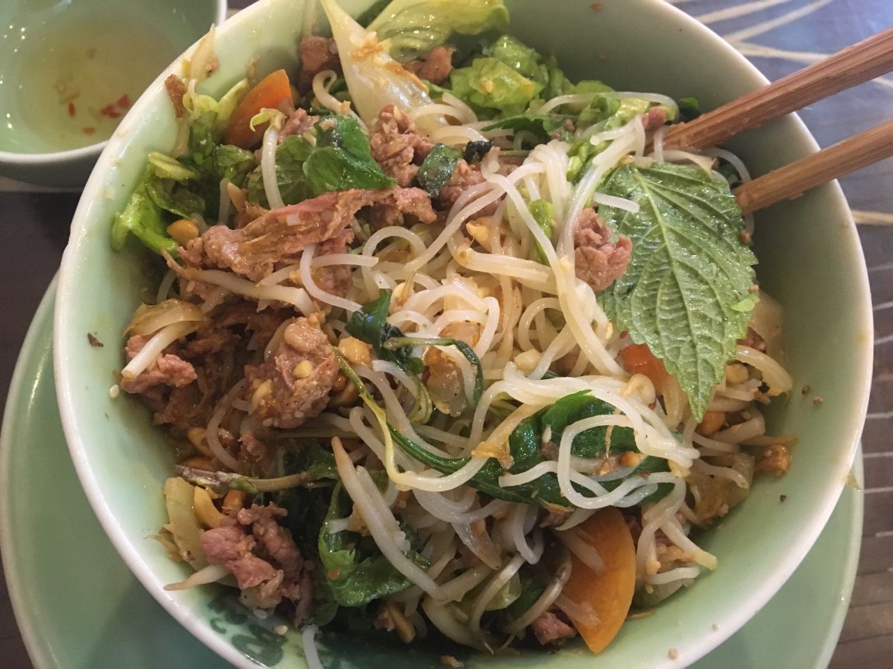 In this broth-free bowl of vermicelli noodles, tender slices of beef mingle with crunchy peanuts, bean sprouts, fresh herbs, crisp dried shallots, a splash of fish sauce and fiery chili pepper.
