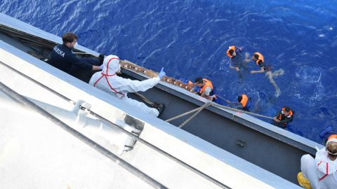 Migrants climb a ladder to the deck of the Italian navy ship.
