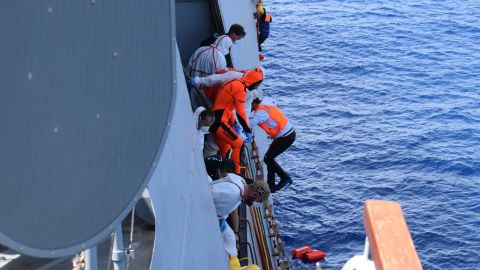 The migrants are helped on board the ship after their own vessel sank.