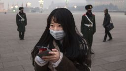 BEIJING, CHINA - DECEMBER 09:  A Chinese woman looks at her phone as Chinese Paramilitary police wear masks to protect against pollution as they stand guard during smog in Tiananmen Square on December 9, 2015 in Beijing, China. The Beijing government issued a "red alert" Sunday for the first time since new standards were introduced earlier this year as the city and many parts of northern China were shrouded in heavy pollution. Levels of PM 2.5, considered the most hazardous, crossed 400 units in Beijing, lower then last week, but still nearly 20 times the acceptable standard set by the World Health Organization. The governments of more than 190 countries are meeting in Paris to set targets on reducing carbon emissions in an attempt to forge a new global agreement on climate change.  (Photo by Kevin Frayer/Getty Images)