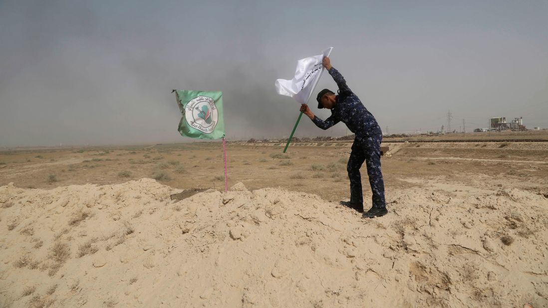 A police officer places an Iraqi federal police flag next to a Shiite militia flag outside Falluja on May 28.