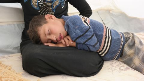 Aus, 7, sleeping on his mother's lap at a refugee camp in Iraq