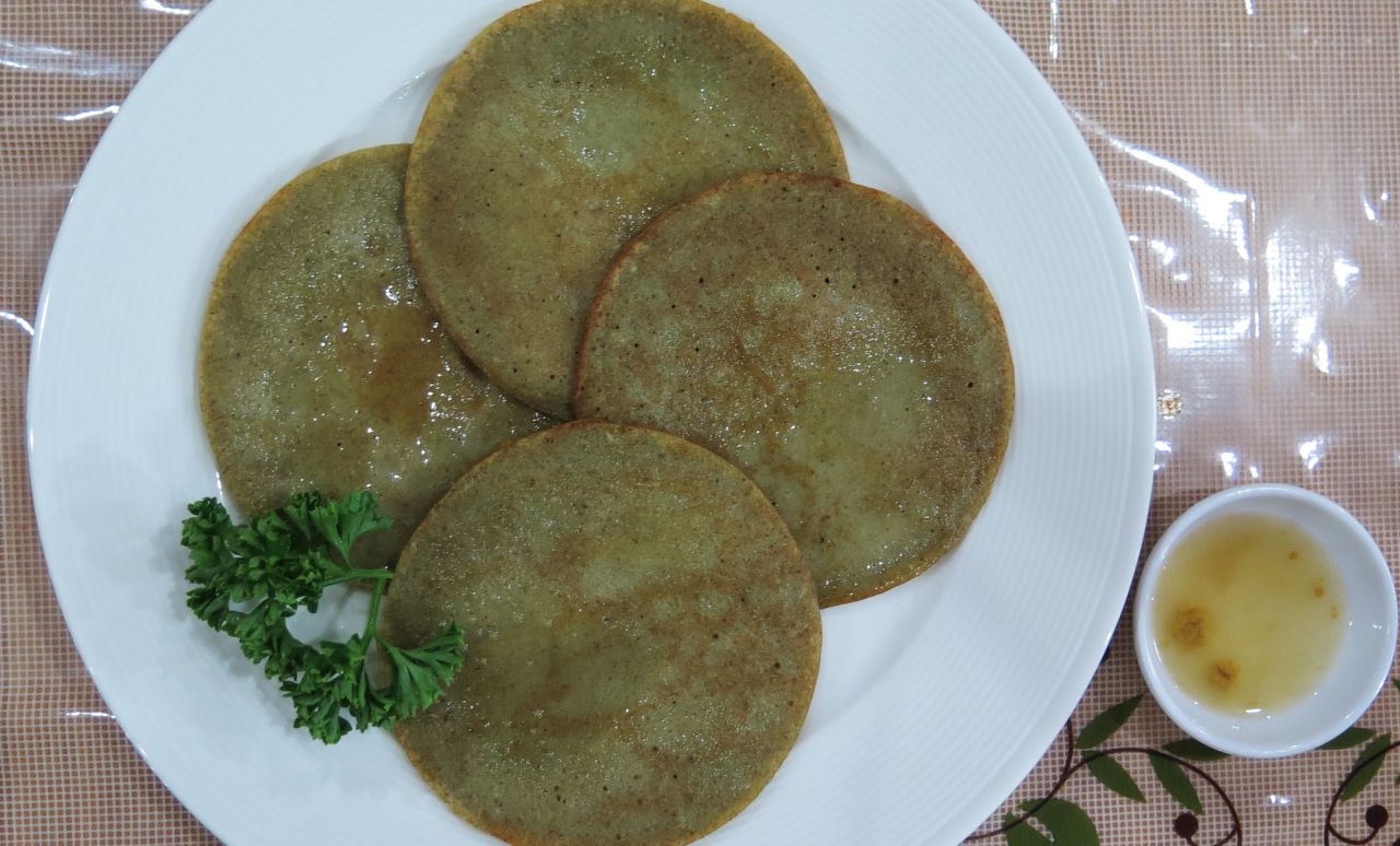 Mung Bean Jijim features four flat, thin, green, circular pancakes, wet with oil and adorned with parsley. 