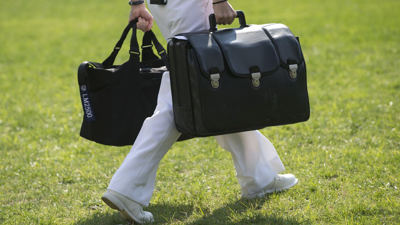A White House military aide and member of the US Navy carries a briefcase known as the "football," containing emergency nuclear weapon codes, as then-President Barack Obama departs from the White House in 2012. 