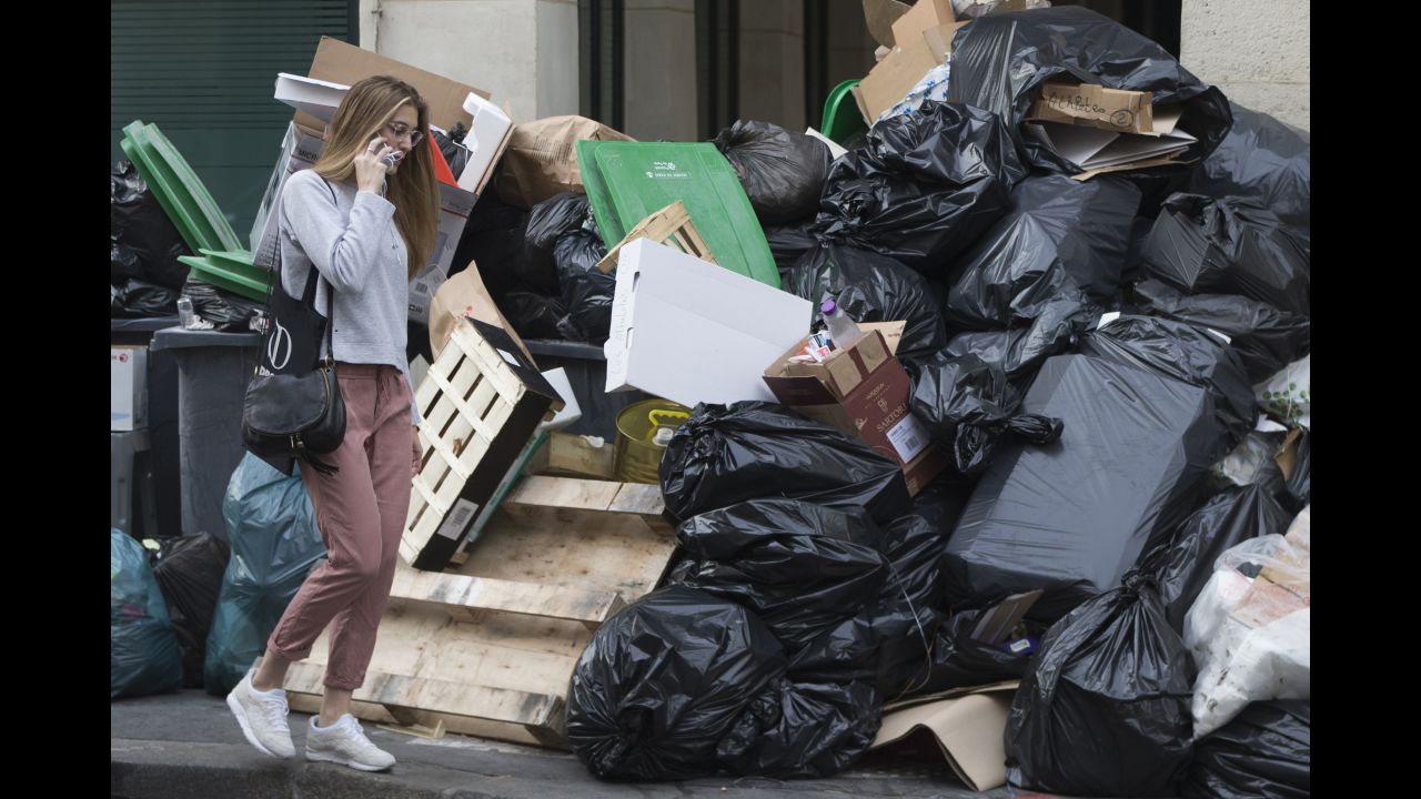 A woman walks past a pile of uncollected rubbish. There has also been a surprise blockade of supply trucks at the main food terminal for the Paris region.