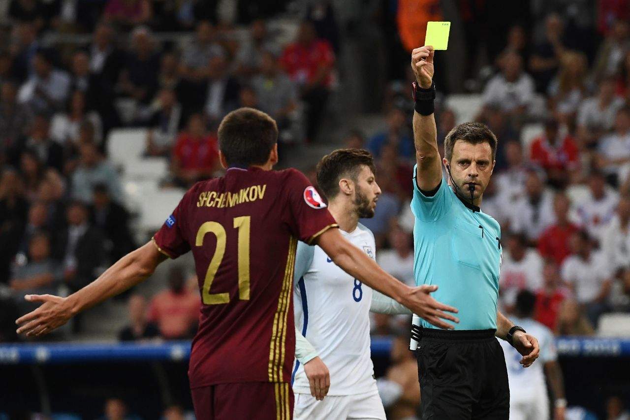 Italian referee Nicola Rizzoli presents Russia defender Georgi Shchenniko, left, with a yellow card.