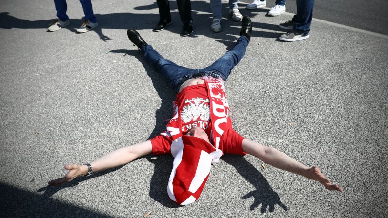 A Poland fan lies on the ground next to friends after they arrived to watch the game in Nice.