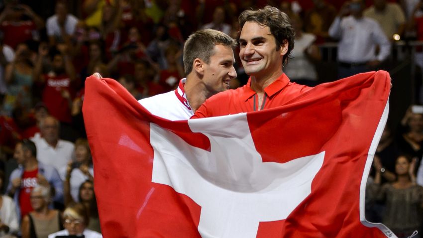Switzerland's Roger Federer (R) waves his national flag next to teammate Michael Lammer as they celebrate winning the Davis Cup semi-final between Switzerland and Italy on September 14, 2014 in Geneva. AFP PHOTO / FABRICE COFFRINI        (Photo credit should read FABRICE COFFRINI/AFP/Getty Images)
