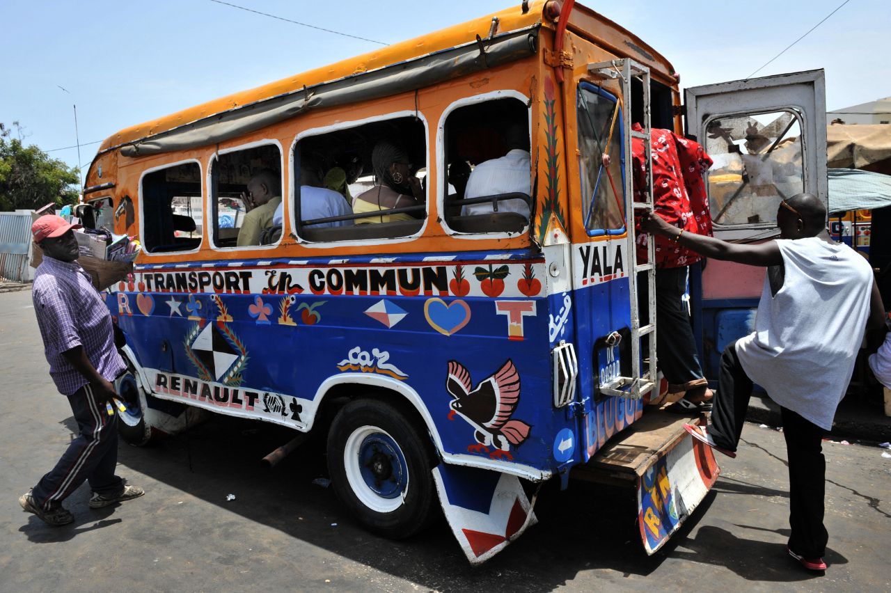 People boarding a car rapides bus, the distinctive yellow and blue buses of Dakar  are decorated with bright images or praise for religious leaders. 