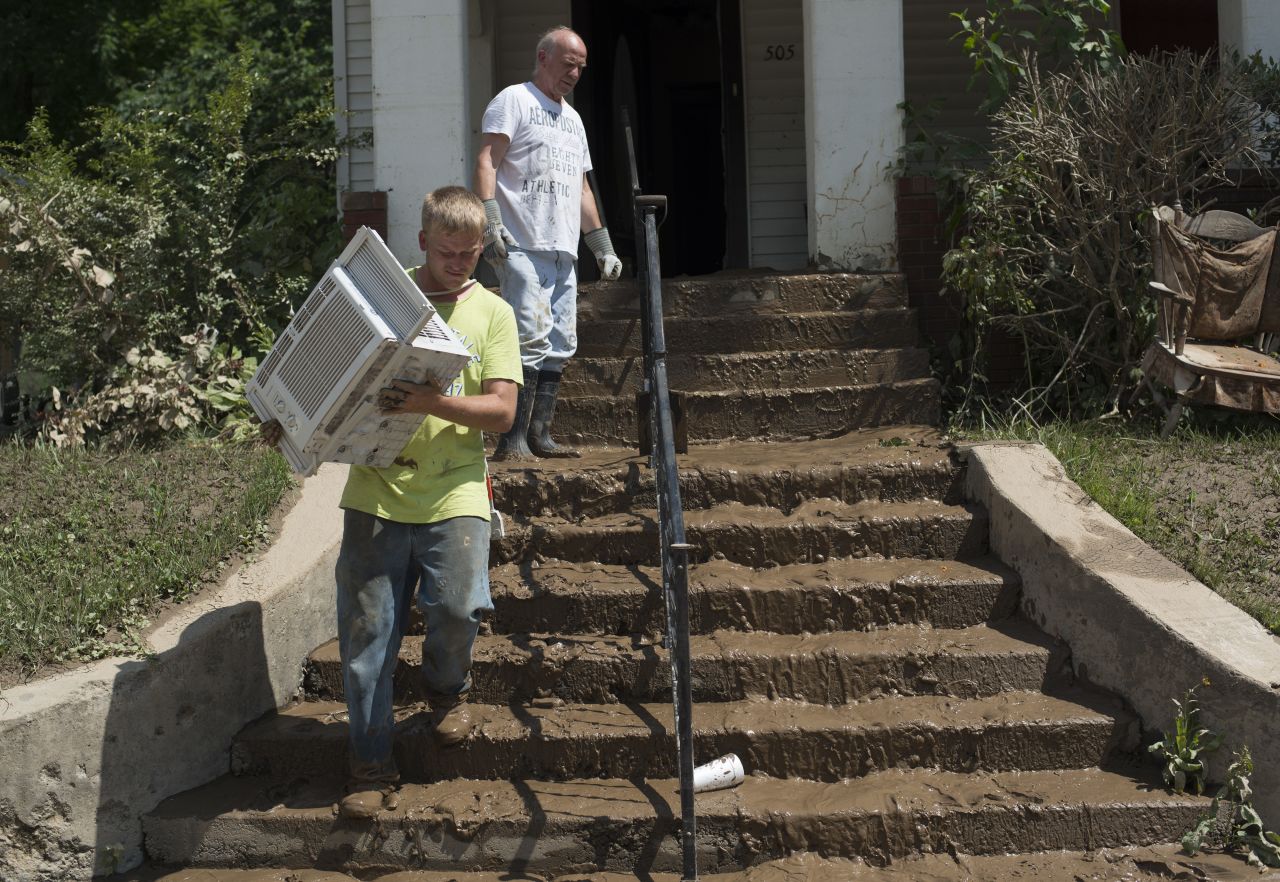 People carry personal belongings down the mud-covered steps of their home in Clendenin on June 25.