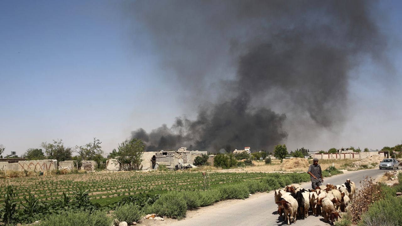 A young Syrian shepherd leads his flock on June 14, as smoke billows from a farm following a reported airstrike in Sheifuniya, near the rebel-held town of Douma, east of the capital Damascus.