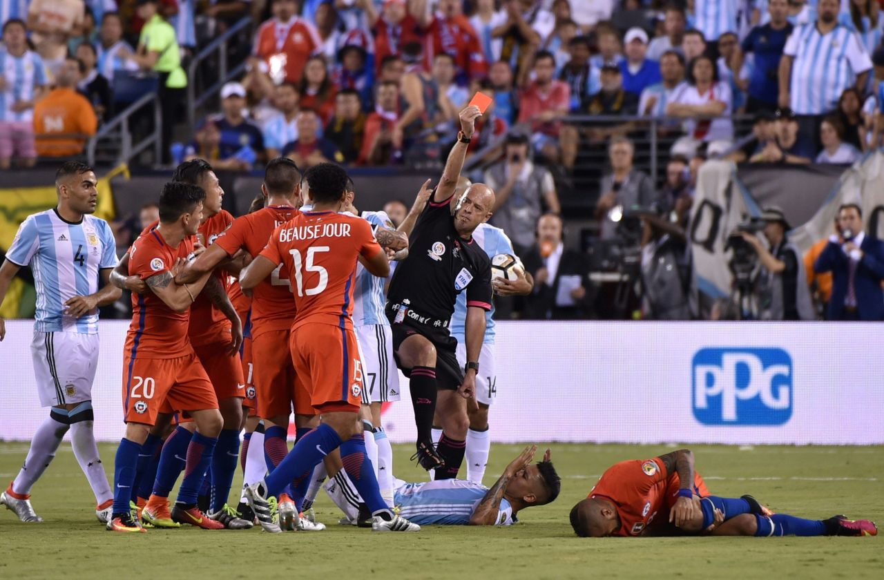 Brazilian referee Heber Lopes red-cards Argentina's Marcos Rojo, center on the ground,  for fouling Chile's Arturo Vidal, right on the ground.