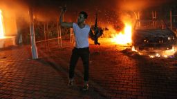 (FILES) This file photo taken on September 11, 2012 shows an armed man waving his rifle as buildings and cars are engulfed in flames after being set on fire inside the US consulate compound in Benghazi.  A long-awaited inquiry into a deadly militant attack on the US mission in the Libyan city of Benghazi late on December 18, 2012 slammed State Department security arrangements there as "grossly inadequate."  But the months-long probe also found there had been "no immediate, specific" intelligence of a threat against the mission, which was overrun on September 11 by dozens of heavily armed militants who killed four Americans.        AFP PHOTO / FILES        (Photo credit should read STR/AFP/Getty Images)