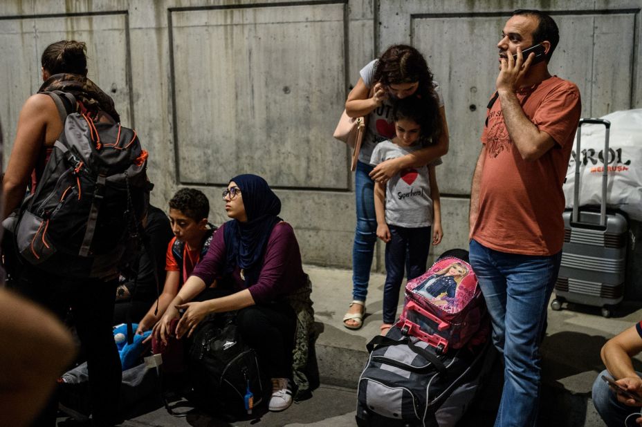 People on their phones wait with their luggage outside the airport.