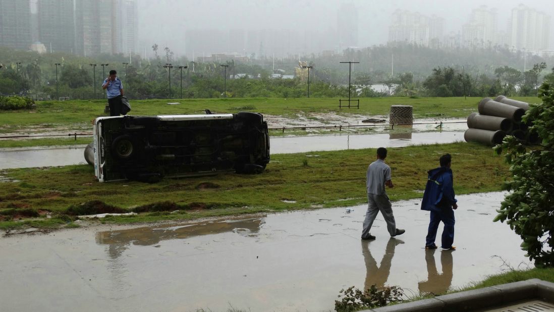 This photograph taken on October 4, 2015 shows people walking past an overturned car after typhoon Mujigae swept the area in Zhanjiang, south China's Guangdong province. Tornadoes spawned by a typhoon that battered southern China left at least seven people dead and more than 200 injured.