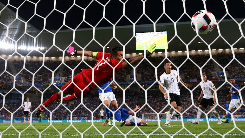 The ball flies past Gianluigi Buffon of Italy as he tries to block Mesut Oezil's opening goal.