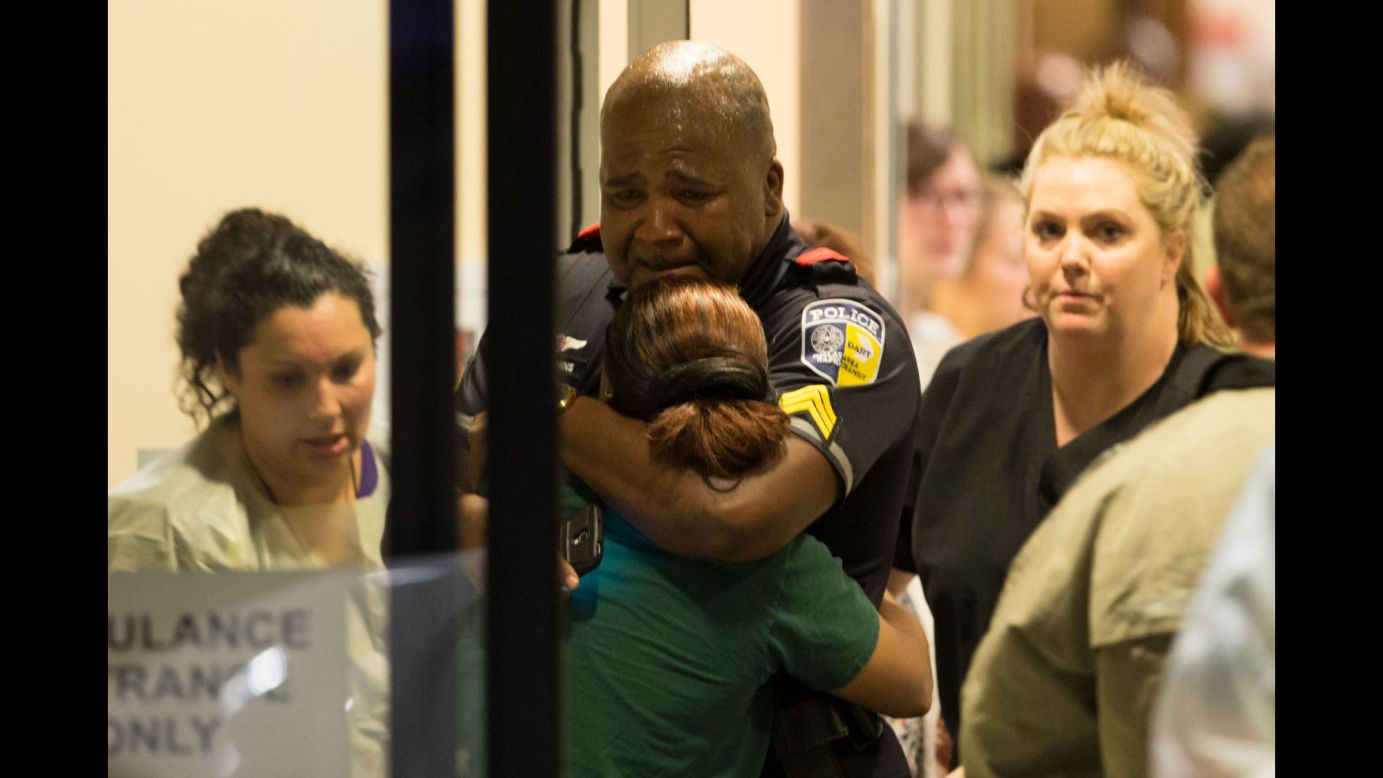 A police officer with Dallas Area Rapid Transit is comforted at the emergency room entrance of the hospital.