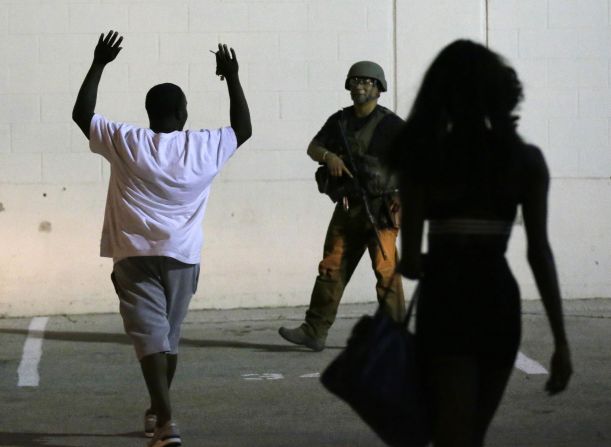 A man raises his hands as he walks near a law enforcement officer in Dallas.