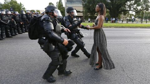 A young woman stands frozen -- clad in a flowing dress, armed only with a cell phone -- in the middle of a street as a pair of police officers move to arrest her. She was one of hundreds of protesters who blocked a Baton Rouge roadway during anti-police brutality demonstrations. The symbolism of a single person's nonviolent resistance against a large, heavily armed opposition is being viewed by some as the photo that symbolizes the week's protests. 