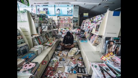 Loong sits in an abandoned store with books and magazines sprawled around him.