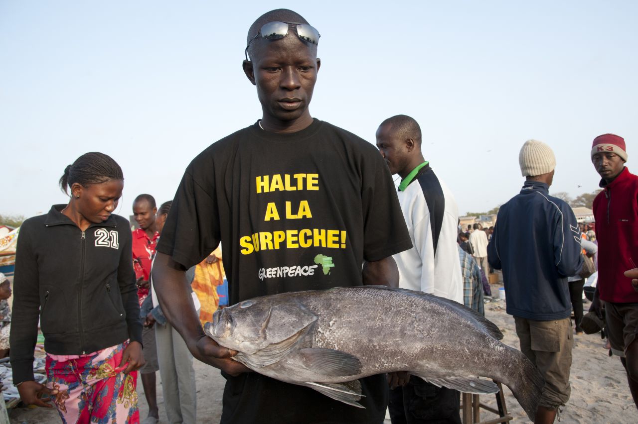 Fish monger with T-shirt reading "stop overfishing" at Soumbedioune fish market in Dakar, Senegal.