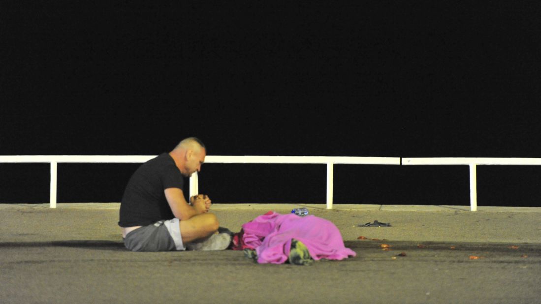 A man sits next to the body of a victim following the attack.