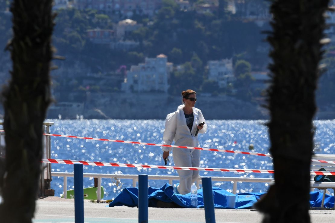 A forensic expert examines dead bodies covered with a blue sheet on the Promenade des Anglais seafront in the French Riviera city of Nice.