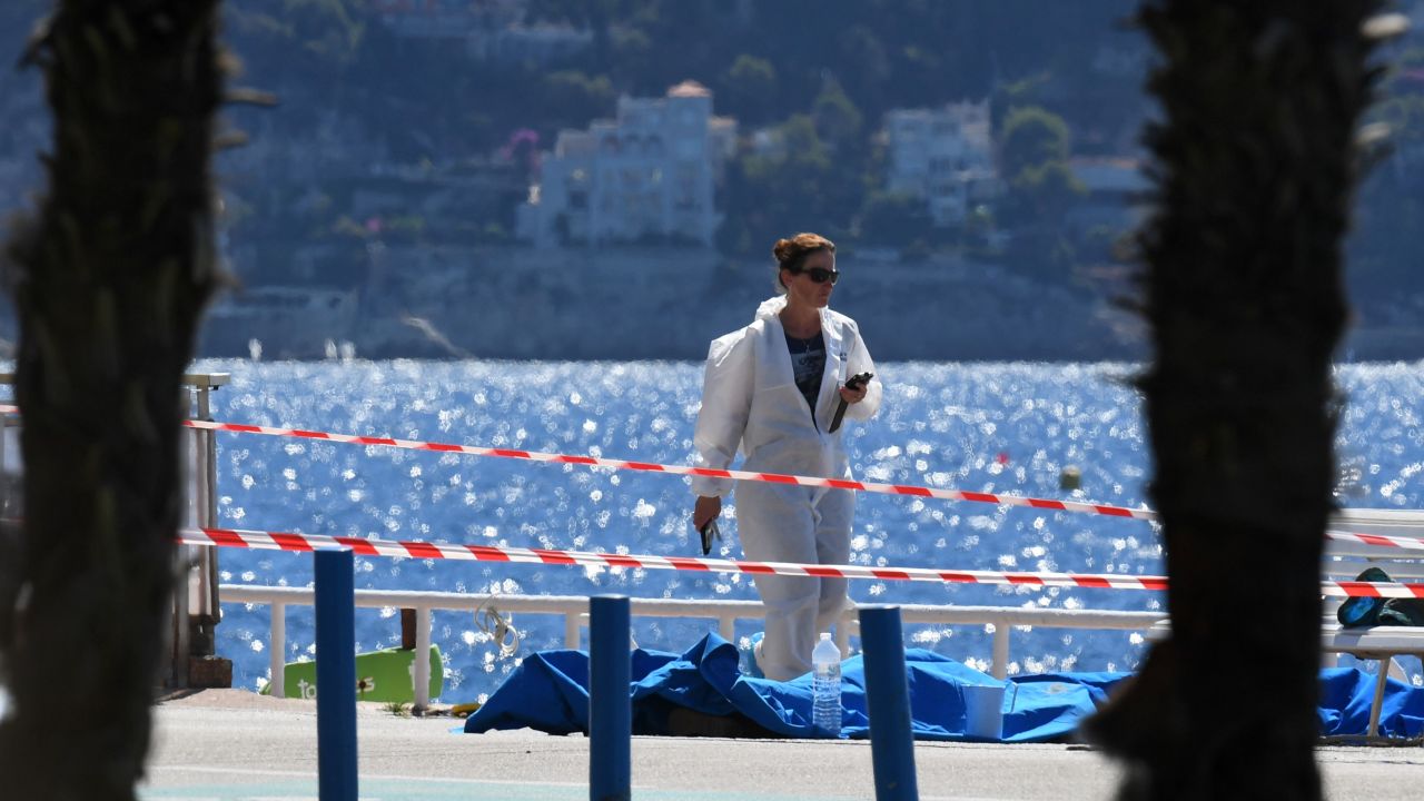 A forensic expert examines dead bodies covered with a blue sheet on the Promenade des Anglais seafront in the French Riviera city of Nice.