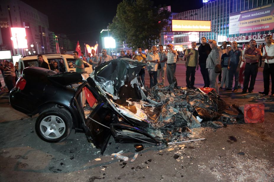 People gather around a car damaged by a tank in Kizilay Square early on July 16. 