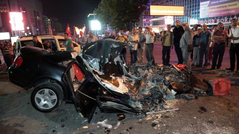 People gather around a car damaged by a tank in Kizilay Square early on July 16.