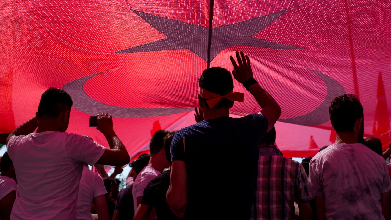 People stand under a huge Turkish flag during a march around Kizilay Square in Ankara in reaction to the attempted coup.