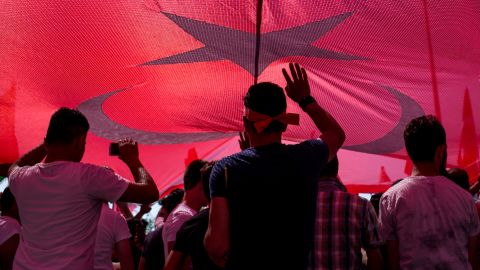 People stand under a huge Turkish flag during a march around Kizilay Square in Ankara in reaction to the attempted coup.