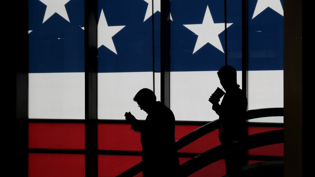 People walk in front of a screen displaying the American flag.