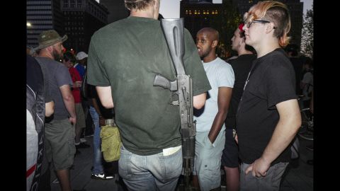 A calm conversation takes place in Public Square with a man wearing a gun.