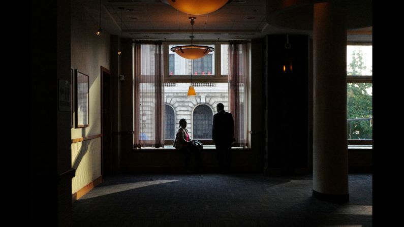 Two people take in the convention scene from a window in a bar.