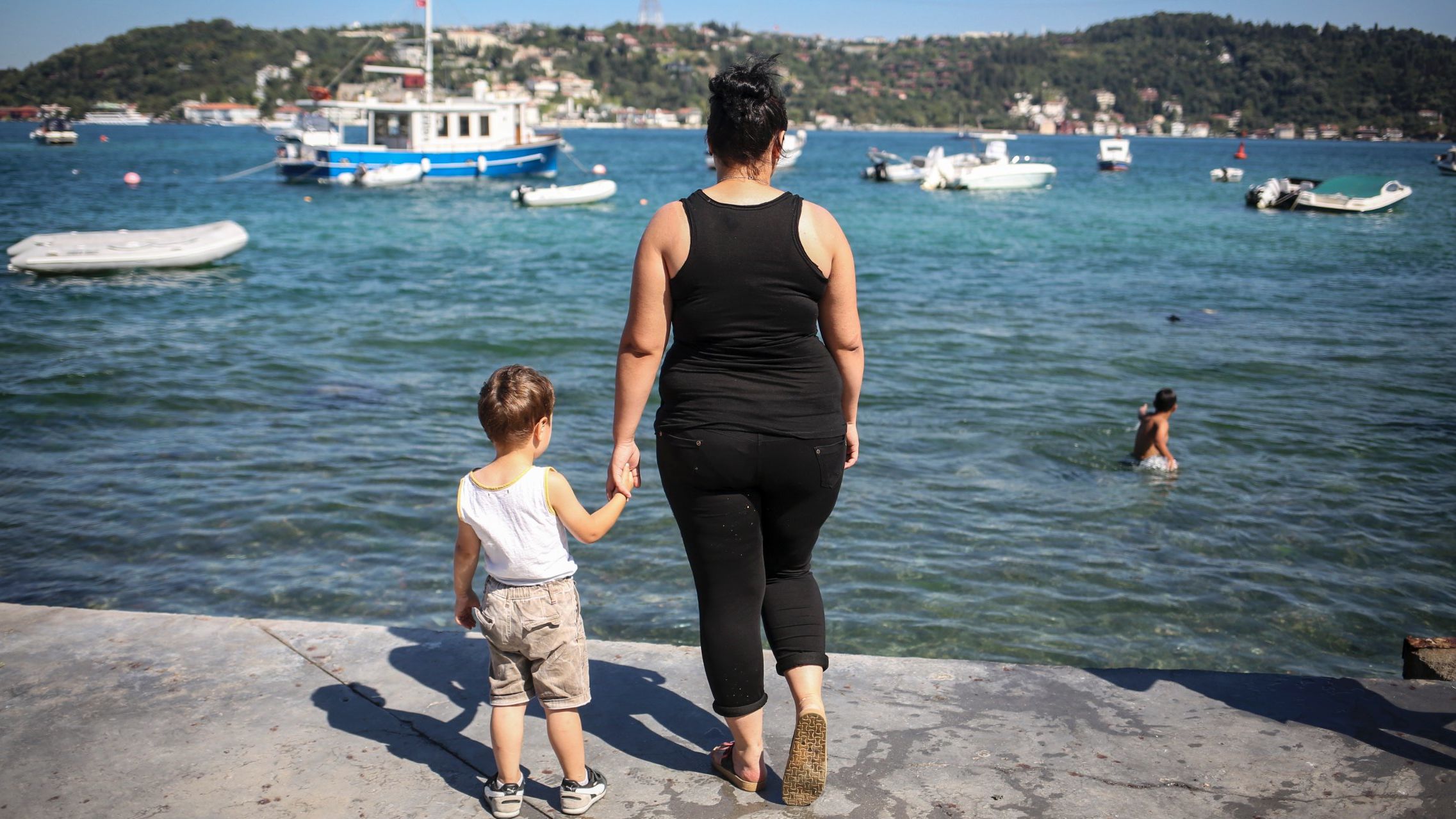 Damla, an unemployed high school dropout, hold's her son's hand as she poses for a photo next to the Bosphorous, in Istanbul. 