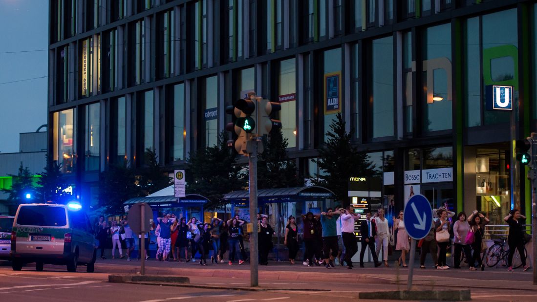 Police officers escort people from the mall with their hands raised.